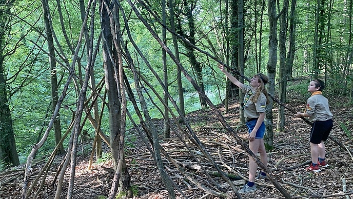 Eine Pfadfinderin und ein Wölfling lehnen den langen Ast an einen Baum