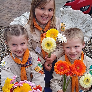 Bunte Blumen, Gesang und lachende Kinderaugen Drei junge Pfadfinder lachen und strecken Blumen in die Kamera